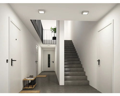 Modern, ljus hall med vita dörrar, en grå betongtrappa och kvadratiska LED-taklampor.
