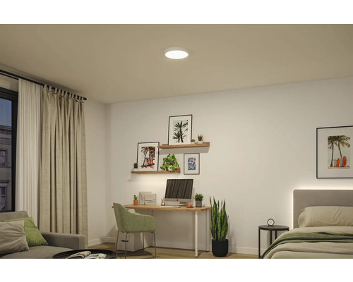 Rund LED-taklampa i ett ljust, modernt inrett rum med skrivbord, vägghyllor och säng.