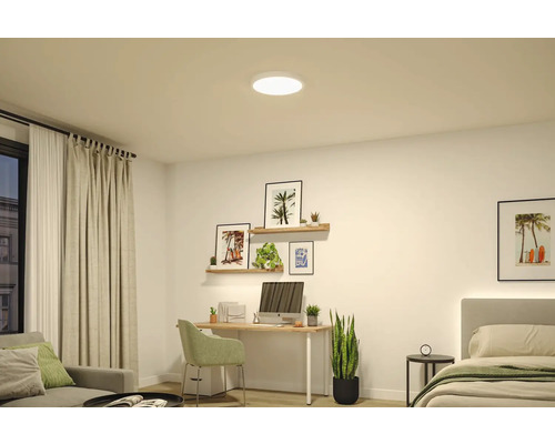 Ljust, modernt rum med en rund vit LED-taklampa, ett skrivbord i trä med dator och vägghyllor med dekoration.