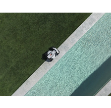 Robotgräsklippare vid kanten av en gräsmatta bredvid en pool med stenram, vy uppifrån.