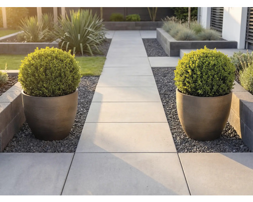 Modern trädgårdsgång av ljusa stenplattor, flankerad av två stora, räfflade planteringskärl med klotformade buxbomar.