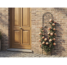 Spaljé av metall med fågel- och bladmotiv, bevuxen med klätterrosor mot en tegelvägg bredvid en trädörr.