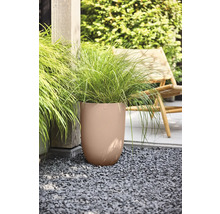 Hög rund planteringskärl med vågig struktur och prydnadsgräs på grus i en trädgård bredvid en trästolpe och en trädgårdsstol.