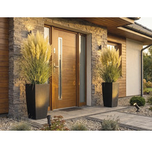 Modern husentré med trädörr, stenbeklädnad och två höga blomkrukor i rottinglook med pampasgräs.