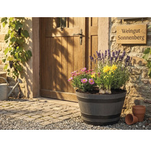 Stort planteringskärl i tunndesign med lavendel, påskliljor och prästkragar framför en rustik trädörr och stenmur.