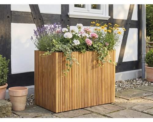 Stor rektangulär planteringslåda av träribbor, planterad med lavendel och pelargoner, på en terrass framför en korsvirkesfasad.