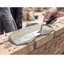 En hand stryker ut murbruk på en tegelvägg med en murarslev på en byggarbetsplats.