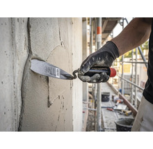 En hantverkare som applicerar murbruk på en betongvägg med en murarslev på en ljus och organiserad byggarbetsplats.