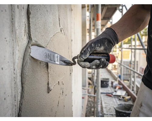 En hantverkare som applicerar murbruk på en betongvägg med en murarslev på en ljus och organiserad byggarbetsplats.