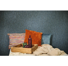 Blå strukturerad tapet i en rumsinteriör med dekorativa kuddar i orange, blått och flerfärgat, en bricka i trä och en stickad filt.