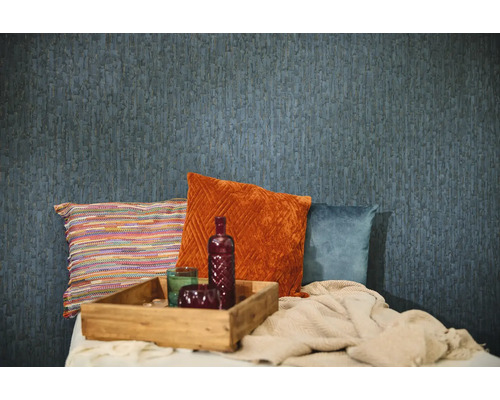 Blå strukturerad tapet i en rumsinteriör med dekorativa kuddar i orange, blått och flerfärgat, en bricka i trä och en stickad filt.