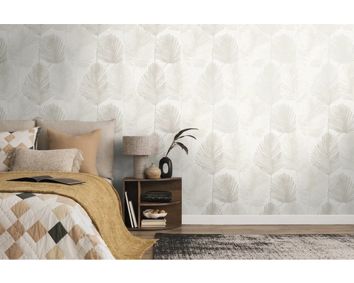 Ljust sovrum med non-woven tapet med palmbladsmönster, en säng med kuddar och ett nattduksbord med lampa.