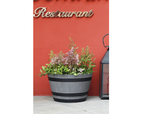 Planteringskärl i fatform med träådring och svarta ringar, planterad med rosa astilbe, placerad bredvid en svart lykta.