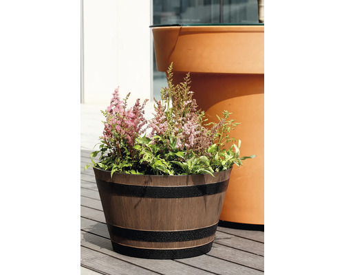 Blomkruka med trälook i form av ett träfat med mörka band, planterad med rosa astilbe på en träterrass.