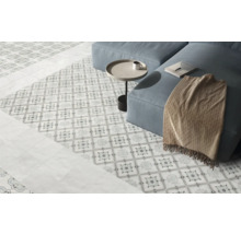 Ljust vardagsrum med dekorativt mönstrat klinkergolv, släta plattor i kantområdet och en soffa.