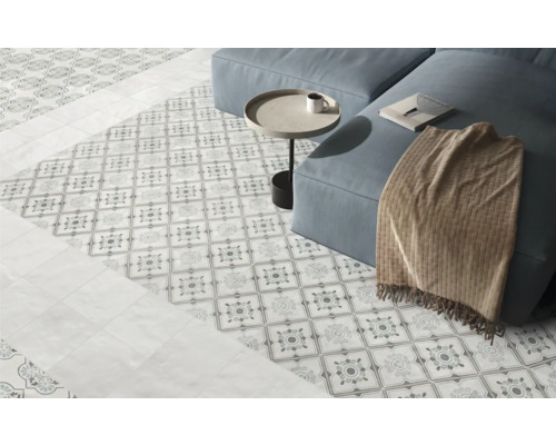 Ljust vardagsrum med dekorativt mönstrat klinkergolv, släta plattor i kantområdet och en soffa.