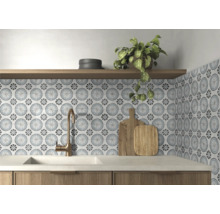 Köksstänkskydd med mönstrat kakel i floral cirkeldesign, bronsfärgad blandare, vit diskho och hylla i trä.