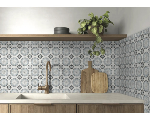Köksstänkskydd med mönstrat kakel i floral cirkeldesign, bronsfärgad blandare, vit diskho och hylla i trä.