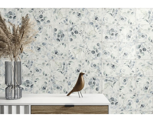 Väggplattor med botaniskt bladmönster i ett ljust rum med glasvas och träfigur på en byrå.