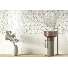 Modernt badrum med blommigt kakel, fristående pelartvättställ, hög guldfärgad blandare, oval spegel och dekorationsvas.