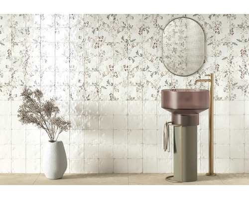 Modernt badrum med blommigt kakel, fristående pelartvättställ, hög guldfärgad blandare, oval spegel och dekorationsvas.