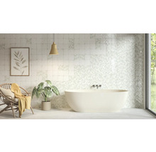 Ljust badrum med fristående badkar och kvadratiskt kakel med blommiga och enkla mönster.