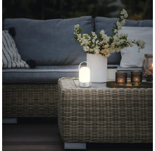 Bärbar LED-bordslampa med varmt ljus på ett rottingbord i en modernt inredd trädgårdslounge med soffa och blommor.