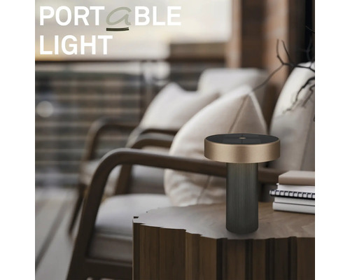 Modern bärbar bordslampa för utomhusbruk på ett sidobord i trä i en organiserad balkongmiljö med loungesstolar och kuddar.