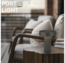 Modern bärbar LED-bordslampa på ett träbord på en uteplats med fåtöljer.