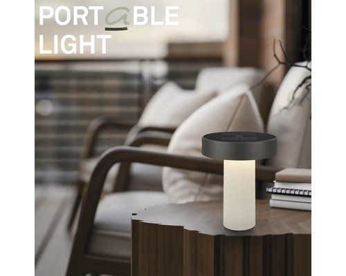 Bärbar LED-bordslampa på ett träbord i en modern utomhusmiljö med bekväma loungestolar.