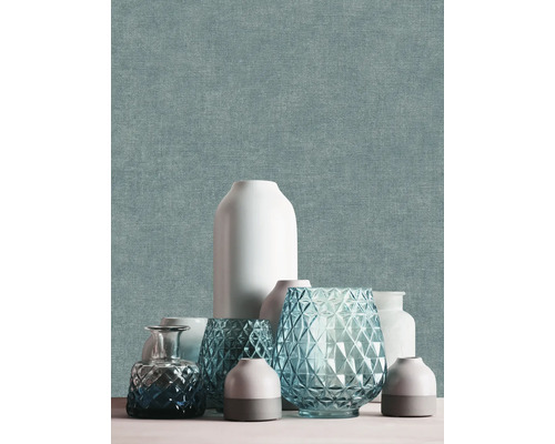 Non-woven tapet med fin textilstruktur i blågrönt, dekorerad med olika vaser i keramik och glas.