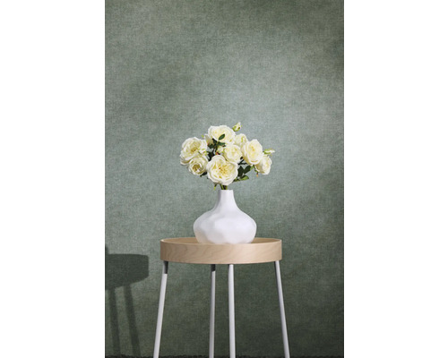 Grön strukturerad non-woven tapet med textiloptik bakom ett sidobord med blomvas.