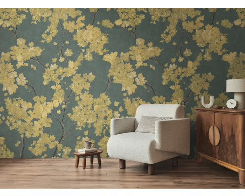 Non-woven fototapet med gula blomgrenar på mörk bakgrund i ett vardagsrum med ljus fåtölj och trämöbler på laminatgolv.