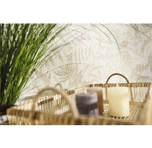 Non-woven tapet med ljust botaniskt bladmöster bakom en dekorativ korg med ljus och grönt gräs.