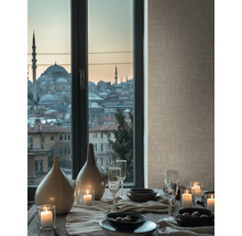 Dukat bord med keramikvaser, tända ljus och glas framför ett fönster med stadsutsikt och beige strukturerad tapet.