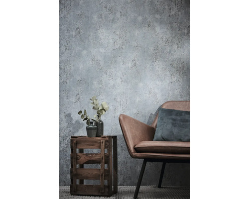 Non-woven tapet med betonglook i ett vardagsrum med en fåtölj i konstläder och en träback som sidobord.