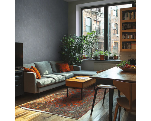 Modernt vardagsrum med grå vägg i betonglook, grå soffa, träbord, orientalisk matta och stora krukväxter framför ett fönster.