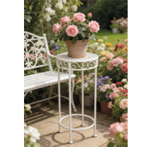 Vit växtställning i metall och vit trädgårdsbänk i en ljus trädgård med blommor på en stenterrass.
