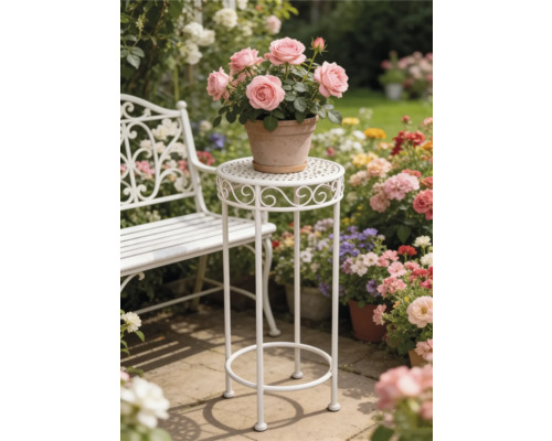 Vit växtställning i metall och vit trädgårdsbänk i en ljus trädgård med blommor på en stenterrass.