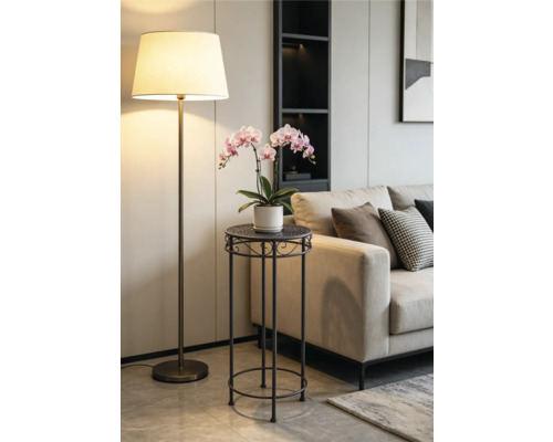 Modernt blombord i metall med en rosa orkidé i ett ljust vardagsrum bredvid en beige soffa och en golvlampa.
