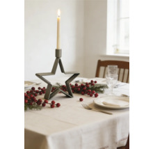 Festligt dukat bord med stjärnformad ljusstake i metall, granris och röda bär på en ljus bordsduk.