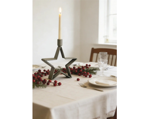 Festligt dukat bord med stjärnformad ljusstake i metall, granris och röda bär på en ljus bordsduk.