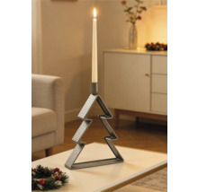 Ljusstake av metall i form av en julgran med ett tänt ljus på ett bord i ett julpyntat vardagsrum.