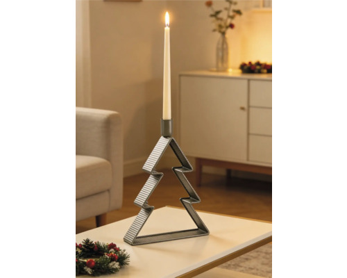 Ljusstake av metall i form av en julgran med ett tänt ljus på ett bord i ett julpyntat vardagsrum.