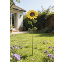 Trädgårdsdekoration solros i metall på en gräsmatta i en ljus trädgård med blommor.