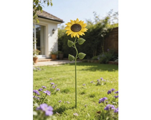 Trädgårdsdekoration solros i metall på en gräsmatta i en ljus trädgård med blommor.