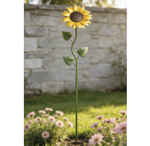 Trädgårdsdekoration solros i metall i en blomrabatt med rosa blommor framför en stenmur.