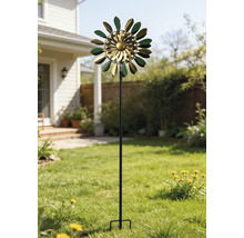 Kinetisk vindsnurra i metall i grönt och guld med bladformade element på en hög stång i en solig trädgård på gräsmattan.