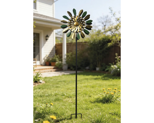 Kinetisk vindsnurra i metall i grönt och guld med bladformade element på en hög stång i en solig trädgård på gräsmattan.