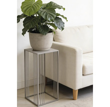 Modernt grått blomställ i metall med minimalistisk design, med en grön växt i kruka bredvid en ljus soffa i ett vardagsrum.